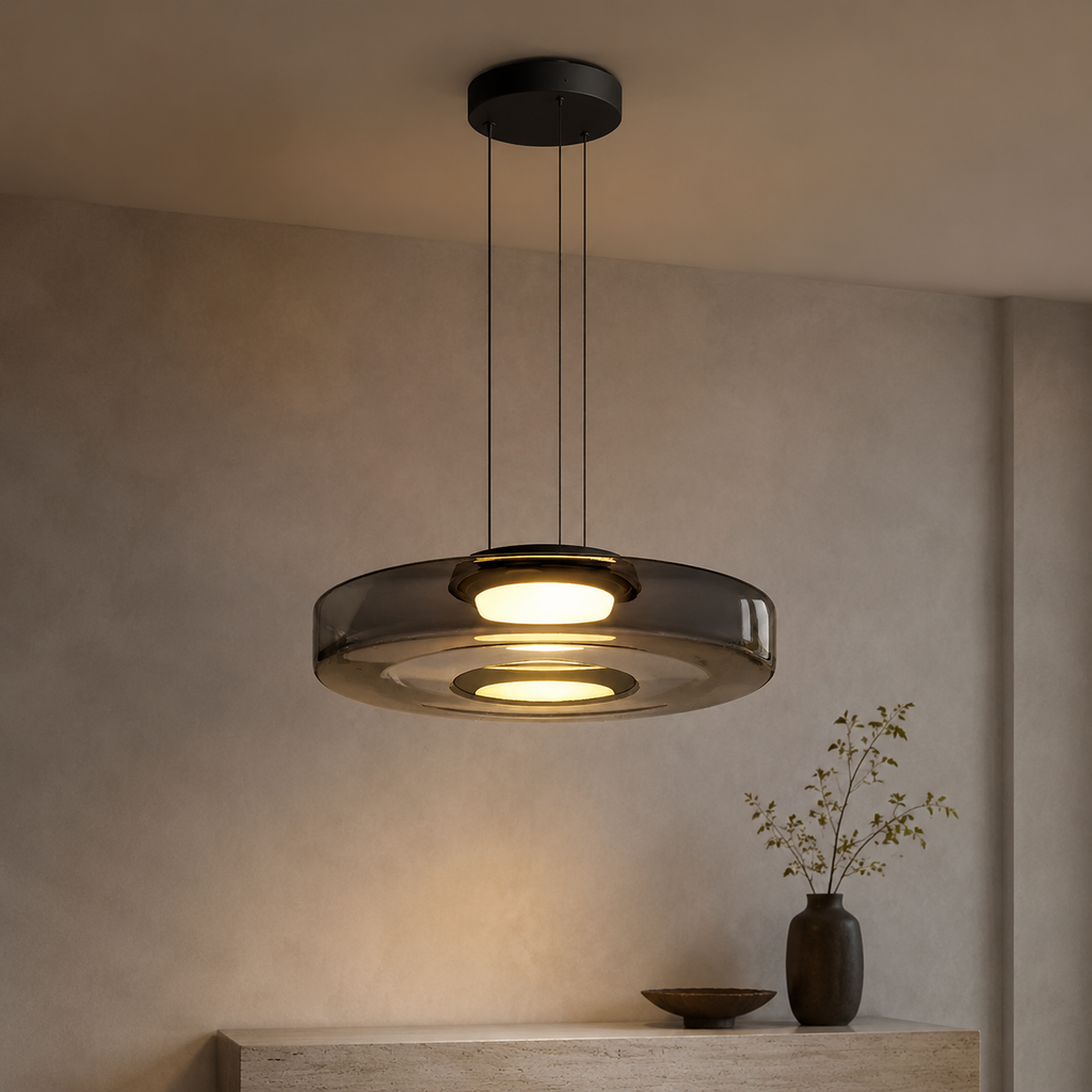 Smoke gray layered glass pendant light hangs lit against a softly textured neutral wall.