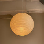 White paper globe pendant light hanging above a furnished living or dining space