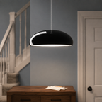 Black dome pendant light suspended near a staircase above a small table.