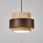 Pendant light with a round travertine and dark wood shade hanging against a light background with the light turned on.