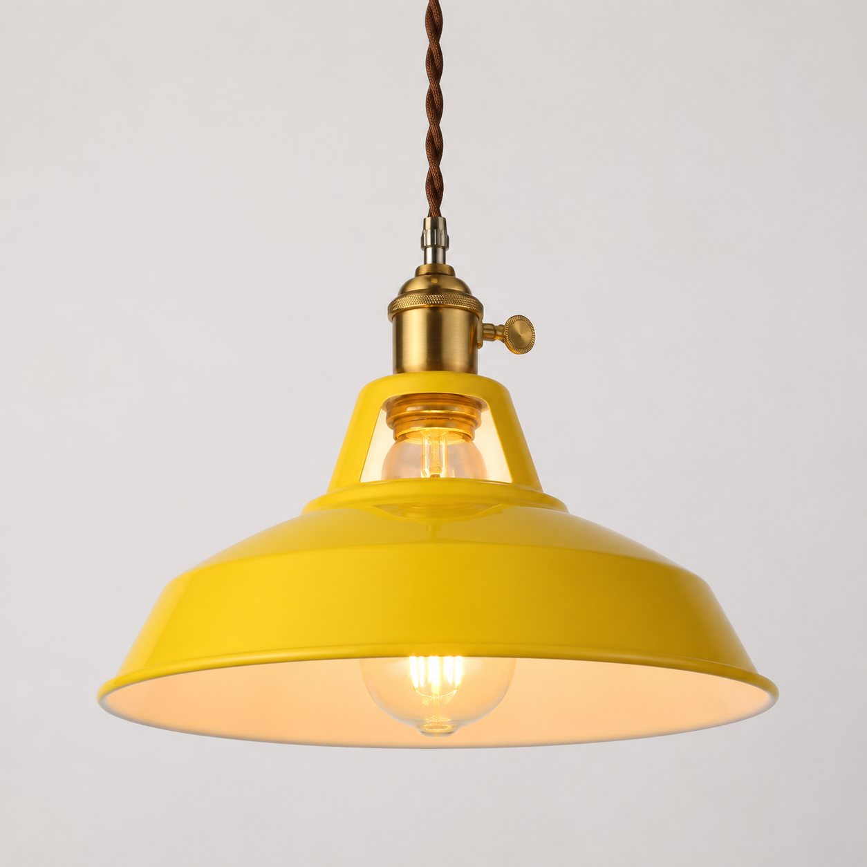 Metal pendant light with a brass socket, twisted brown cord, and exposed warm-glowing bulb.