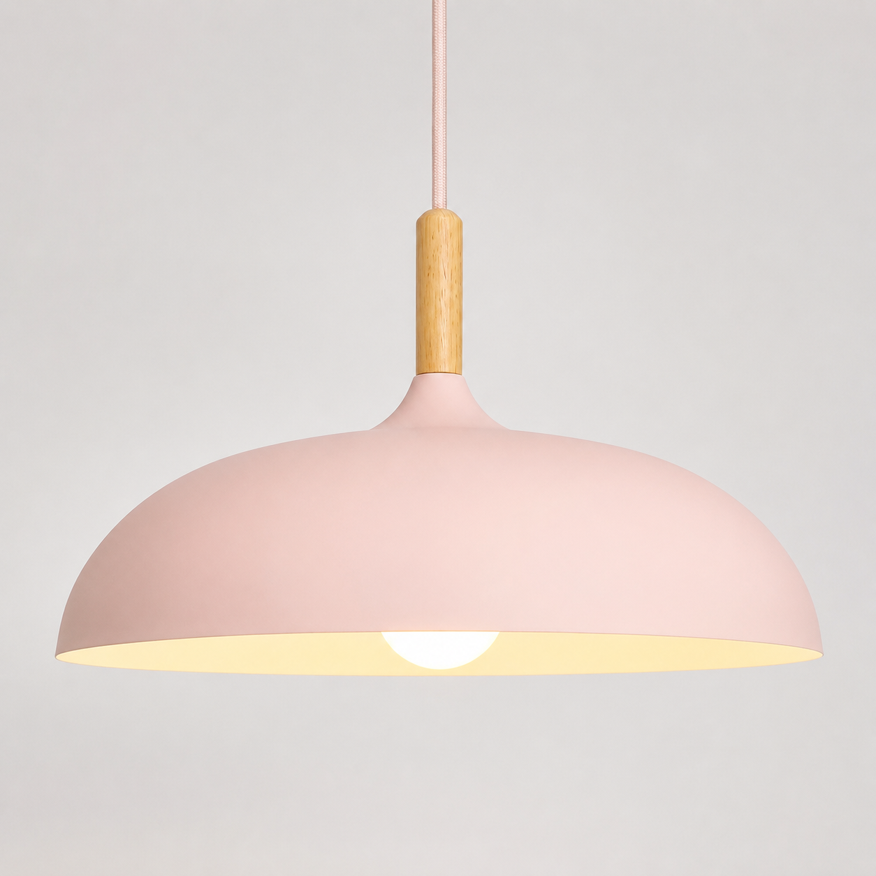 Pink wide-dome pendant light with a natural wood stem, glowing warm white against a neutral background.