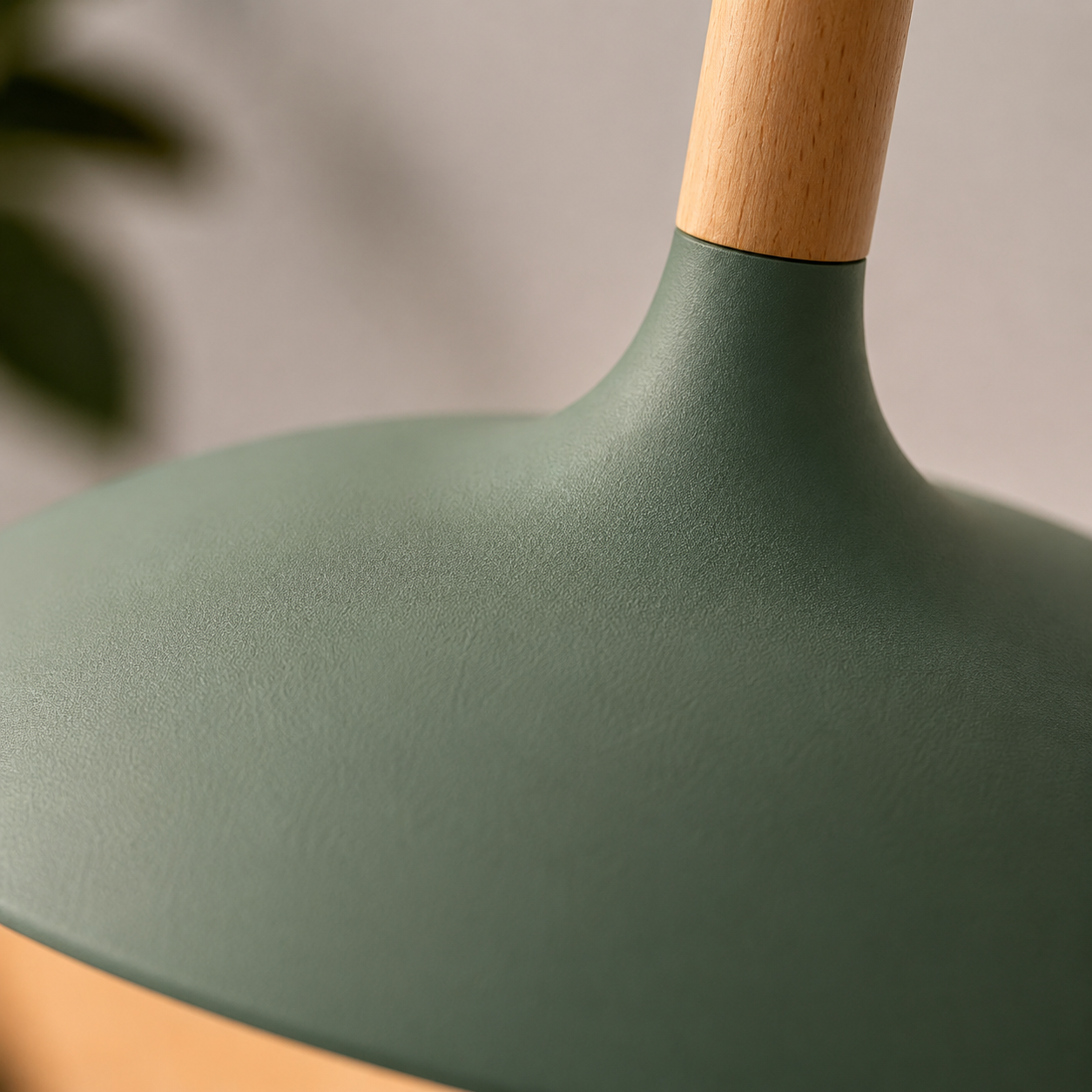 Close-up of a green wide-dome pendant light showing the textured aluminum shade and natural wood stem.
