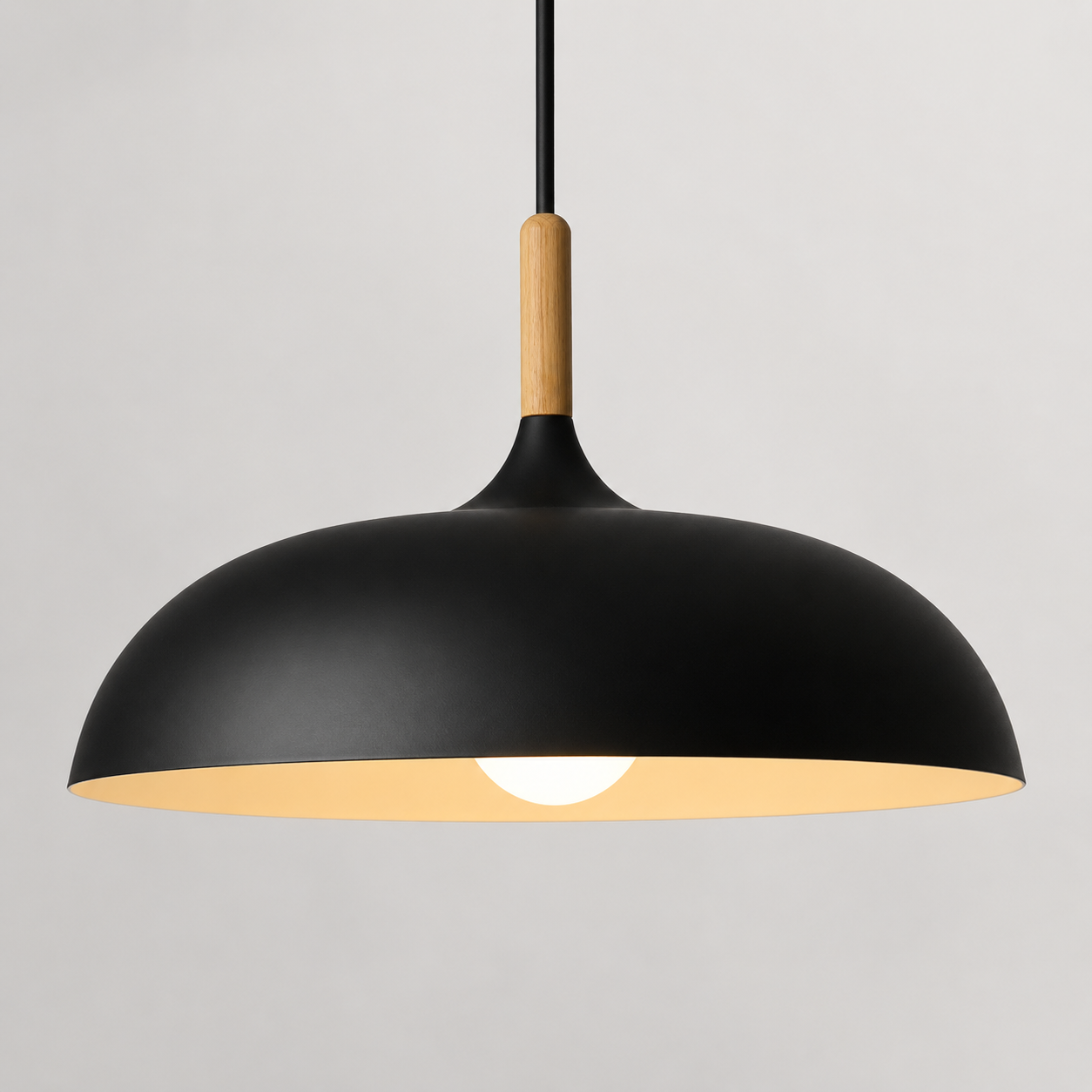 Black wide-dome pendant light with a natural wood stem, glowing warm white against a neutral background.
