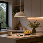 White wide-dome pendant light with a natural wood stem, glowing warm white above a modern kitchen island with pears, a mug, an open book, and a vase.
