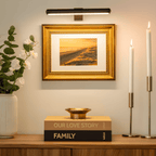 Black picture light illuminating framed artwork above a console.