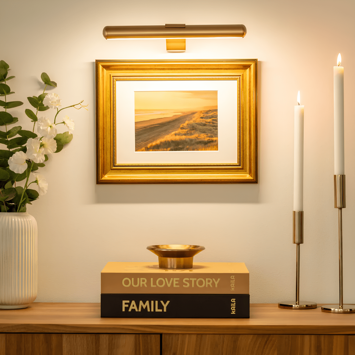 Gold picture light above framed artwork in a styled interior.