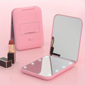 Pink pocket makeup mirror open beside lipstick with LED lights visible.