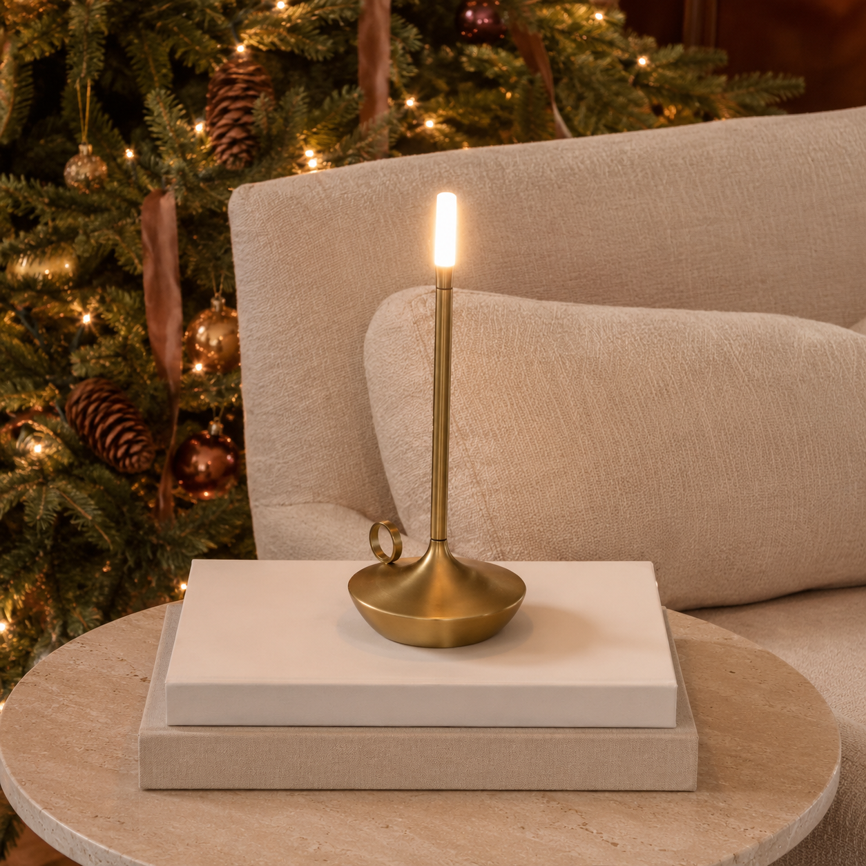 Gold portable table lamp on blank books beside a lit evergreen tree.