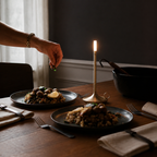 Gold portable table lamp beside plated meals as a hand adds garnish.
