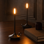 Two black portable table lamps glowing beside blank books and a candle jar.