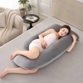 Gray U shaped pregnancy pillow supporting a resting adult on a bed.