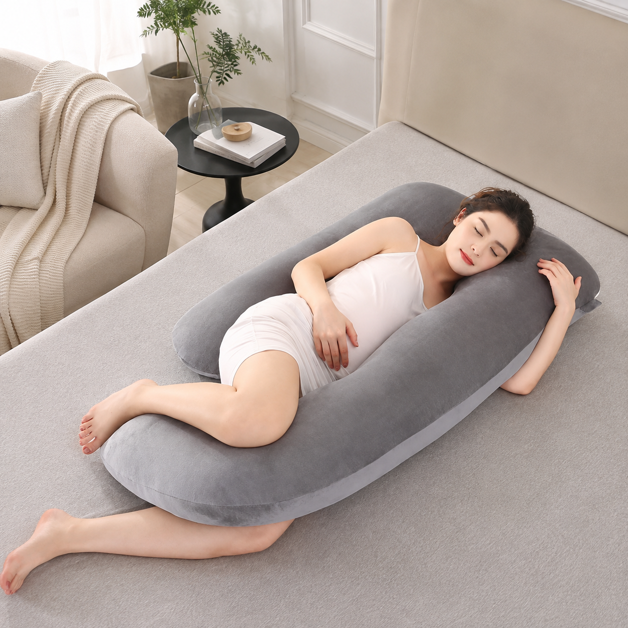 Gray U shaped pregnancy pillow supporting a resting adult on a bed.