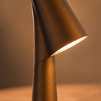 Close-up of the golden brown table lamp head glowing above its tapered body.
