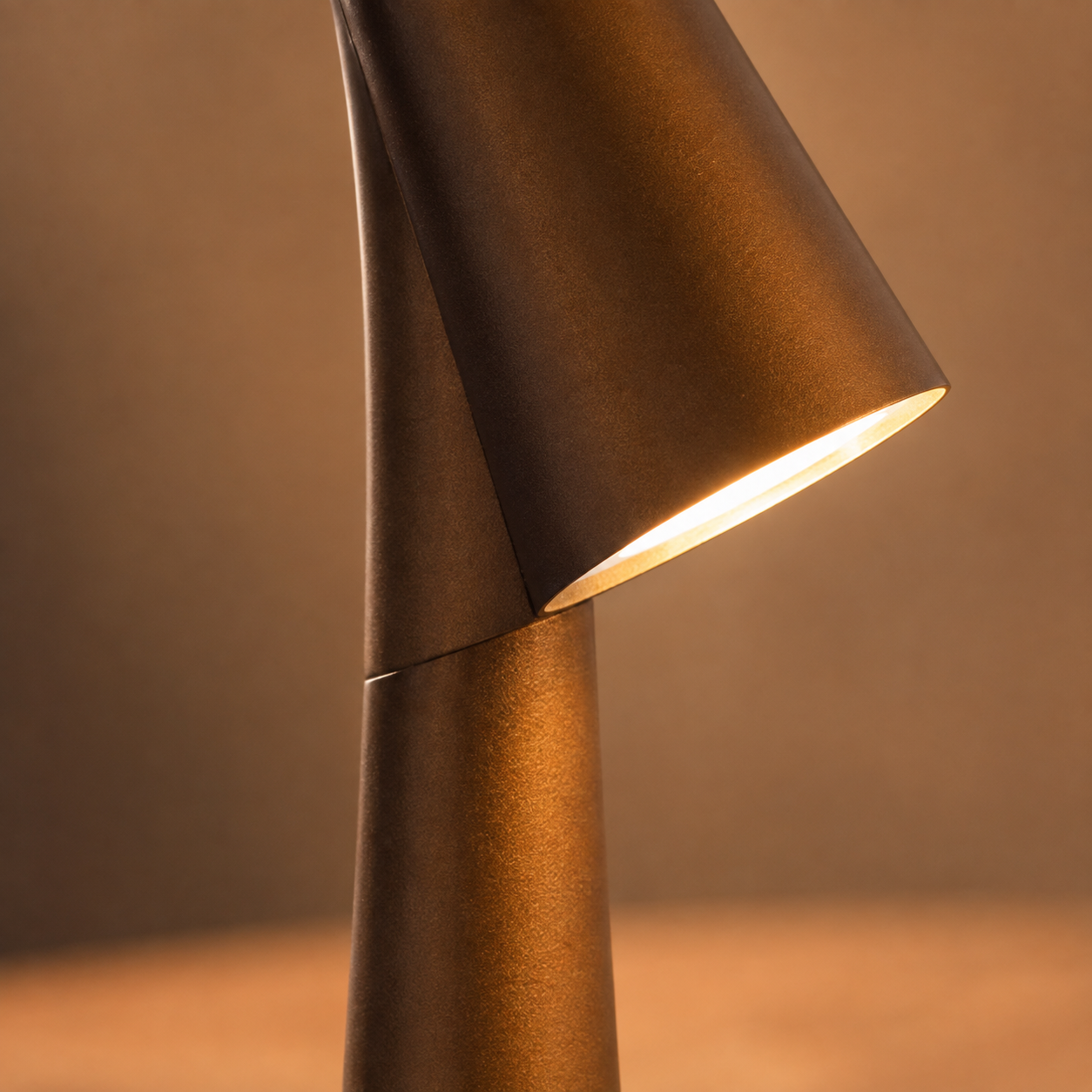 Close-up of the golden brown table lamp head glowing above its tapered body.