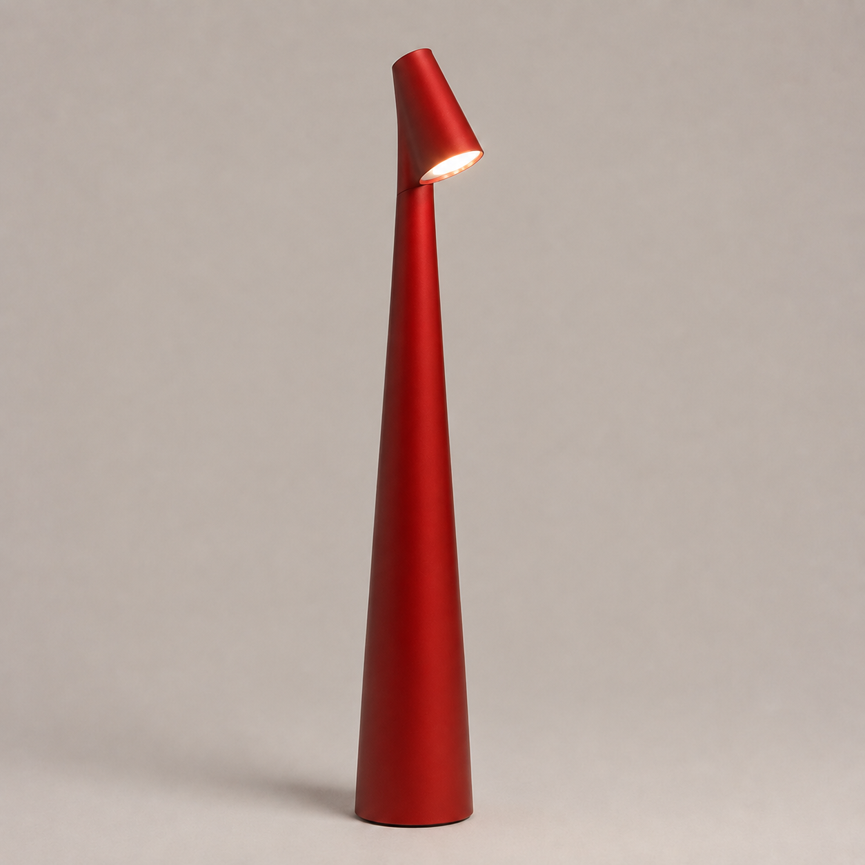 Red table lamp with a tapered cone body and angled light head on a neutral studio background.