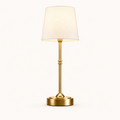 A modern table lamp with a warm gold-finished metal stem and circular base, paired with a tapered off-white fabric shade, shown against a plain white background.