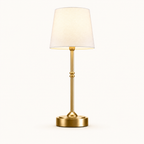 A modern table lamp with a warm gold-finished metal stem and circular base, paired with a tapered off-white fabric shade, shown against a plain white background.