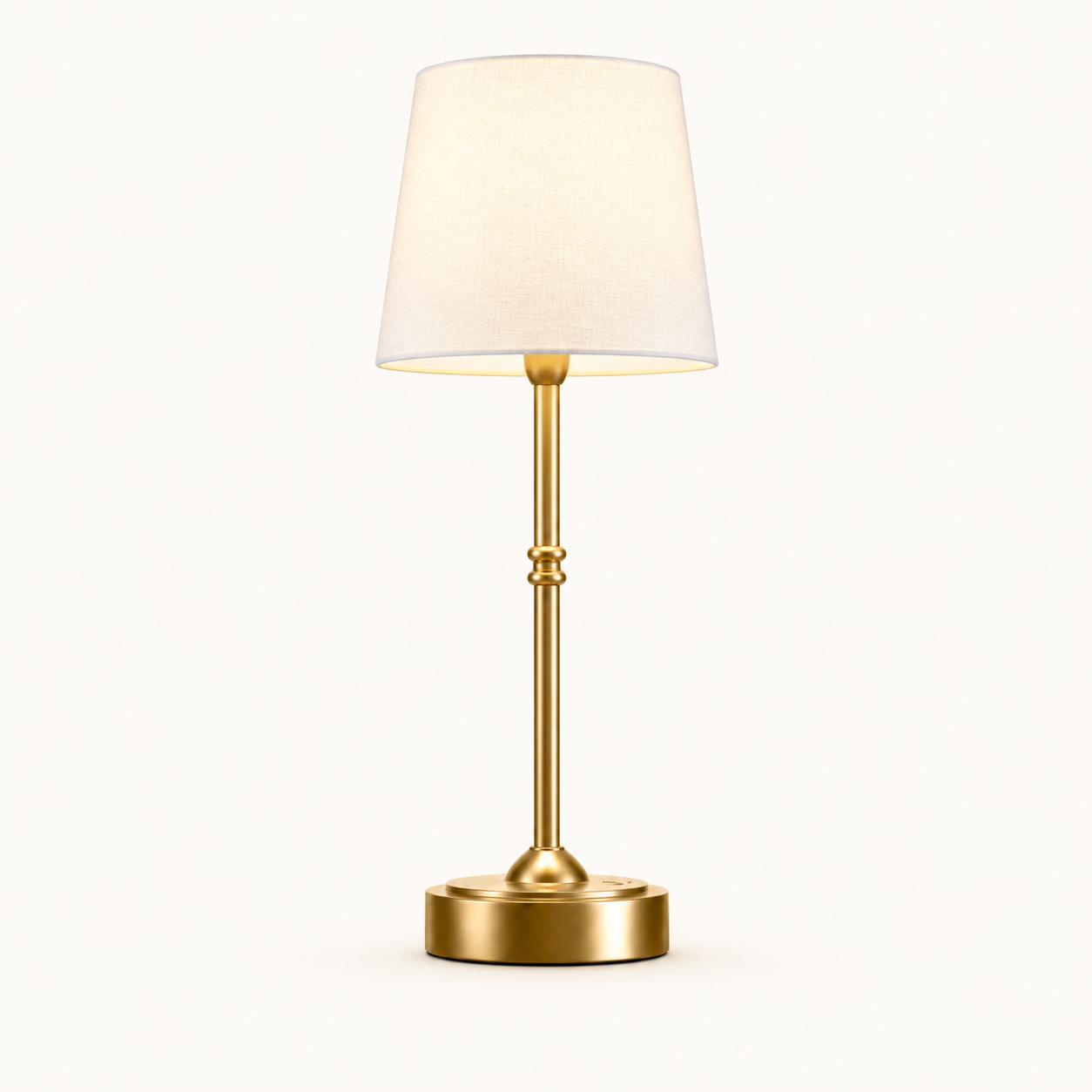 A modern table lamp with a warm gold-finished metal stem and circular base, paired with a tapered off-white fabric shade, shown against a plain white background.