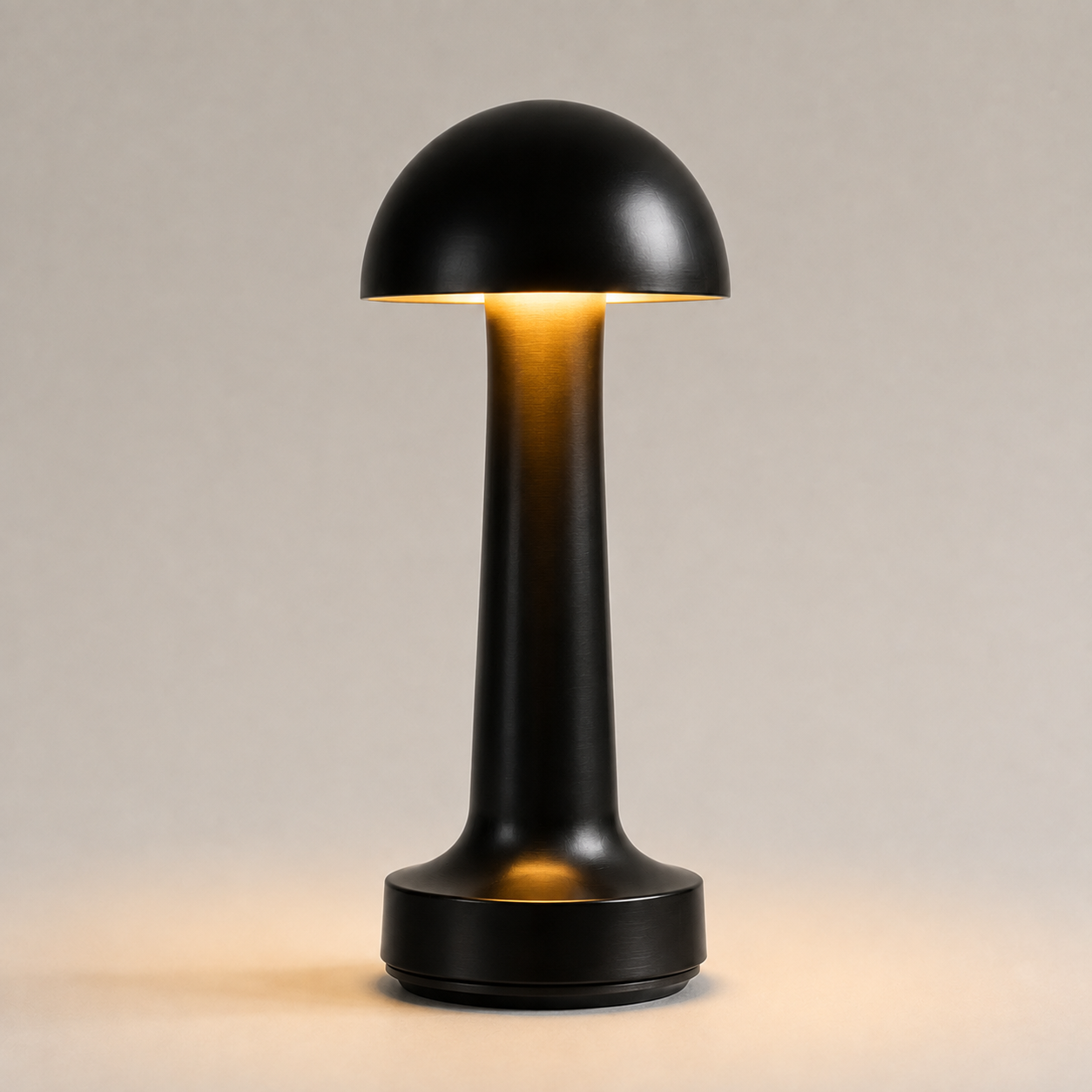 Black dome table lamp glowing on a light neutral studio background.