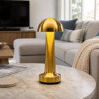Gold dome table lamp glowing on a round table beside a light-colored sofa.