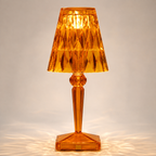 Amber transparent table lamp with a faceted shade and square base on a light background.