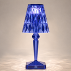 Blue transparent table lamp with a faceted shade and square base on a light background.