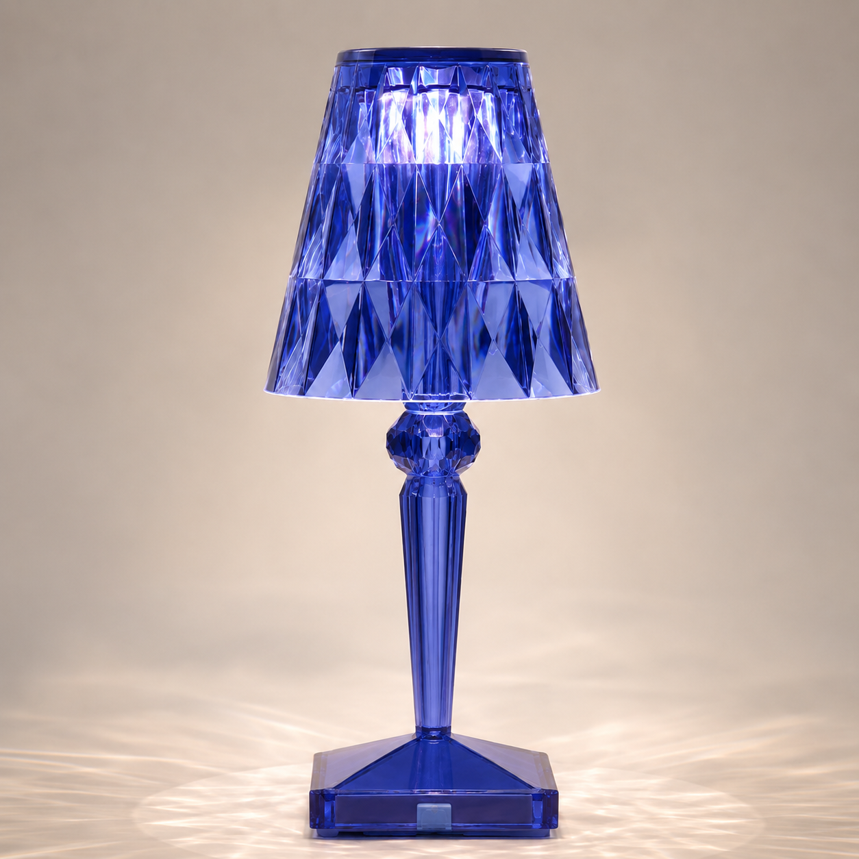 Blue transparent table lamp with a faceted shade and square base on a light background.