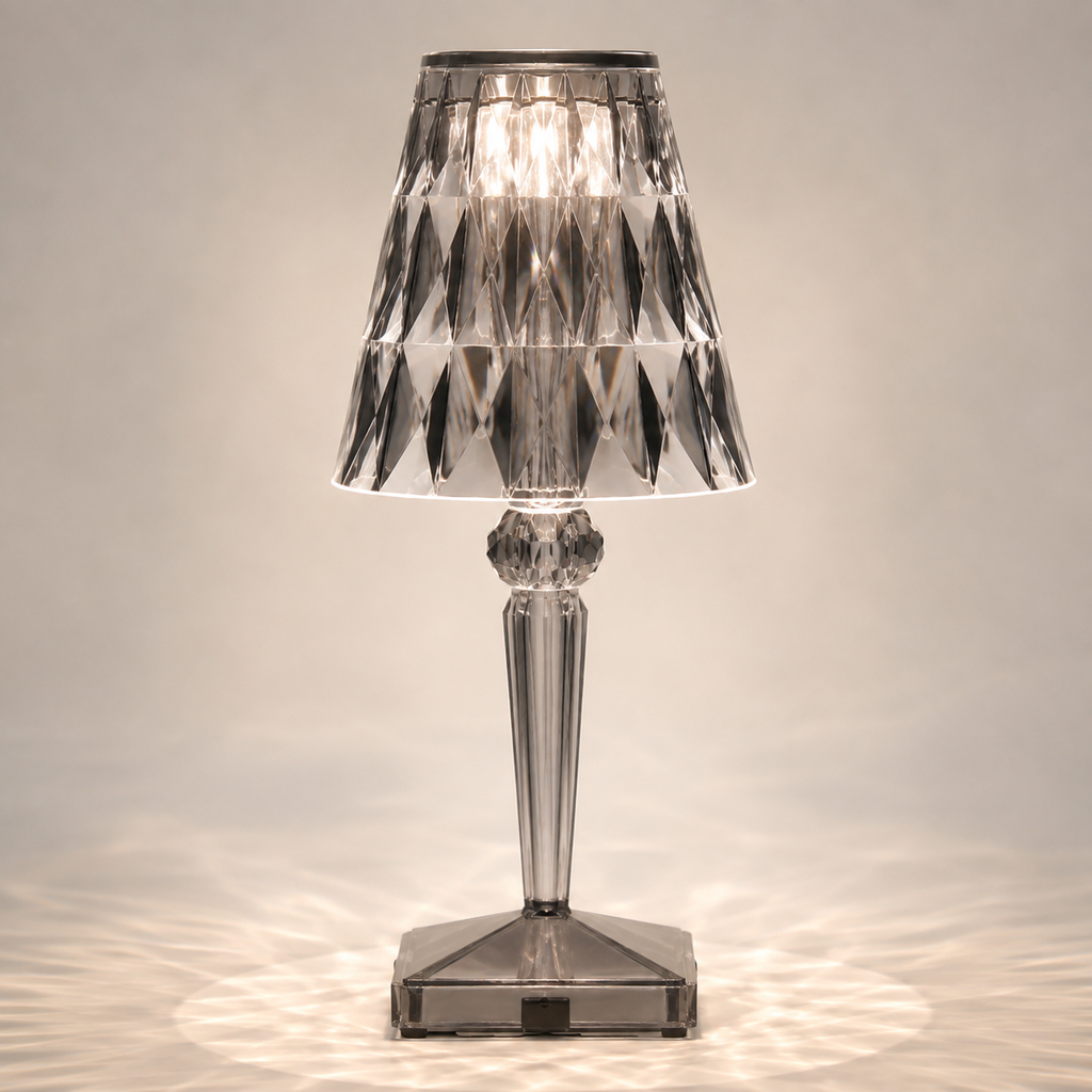 Gray transparent table lamp with a faceted shade and square base on a light background.