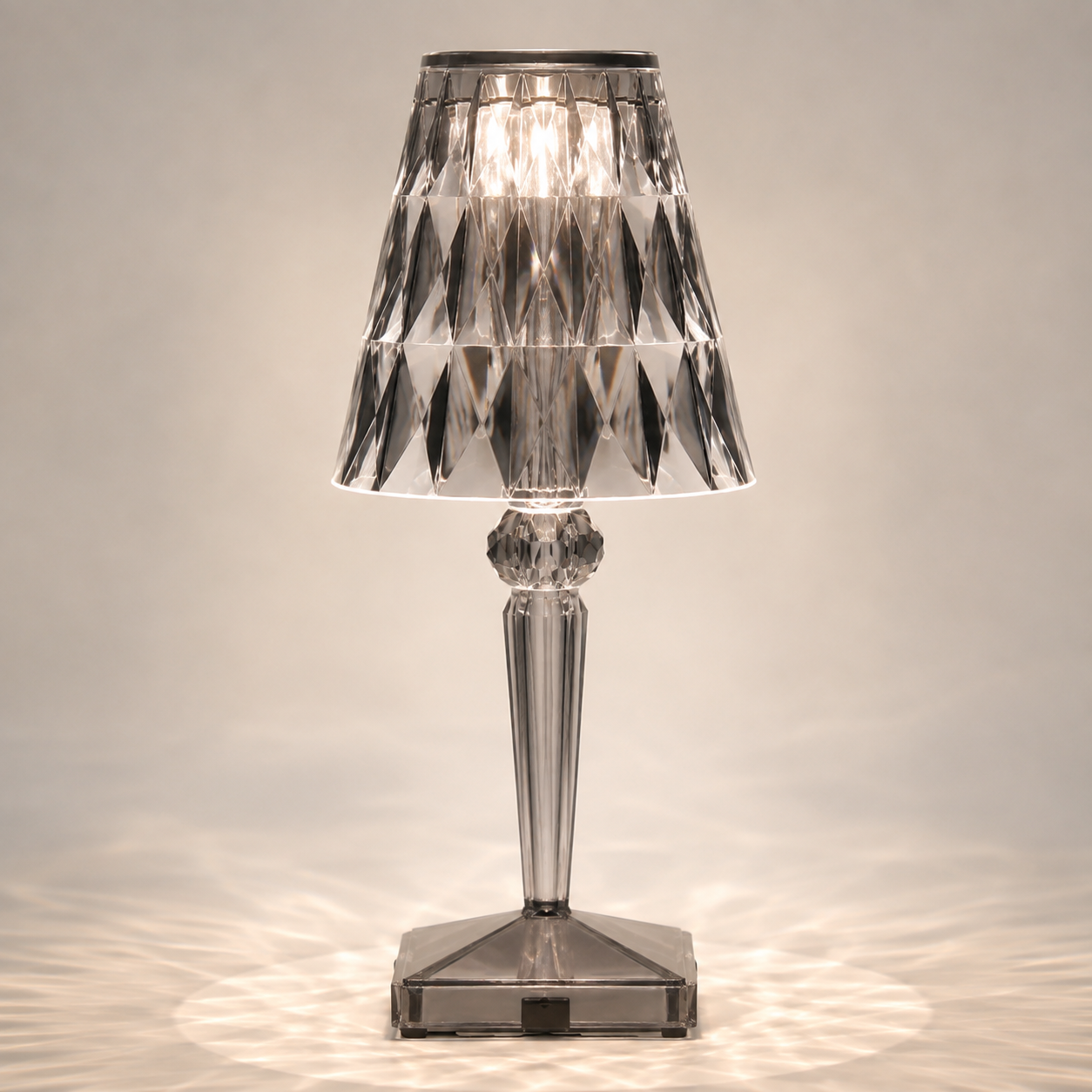 Gray transparent table lamp with a faceted shade and square base on a light background.
