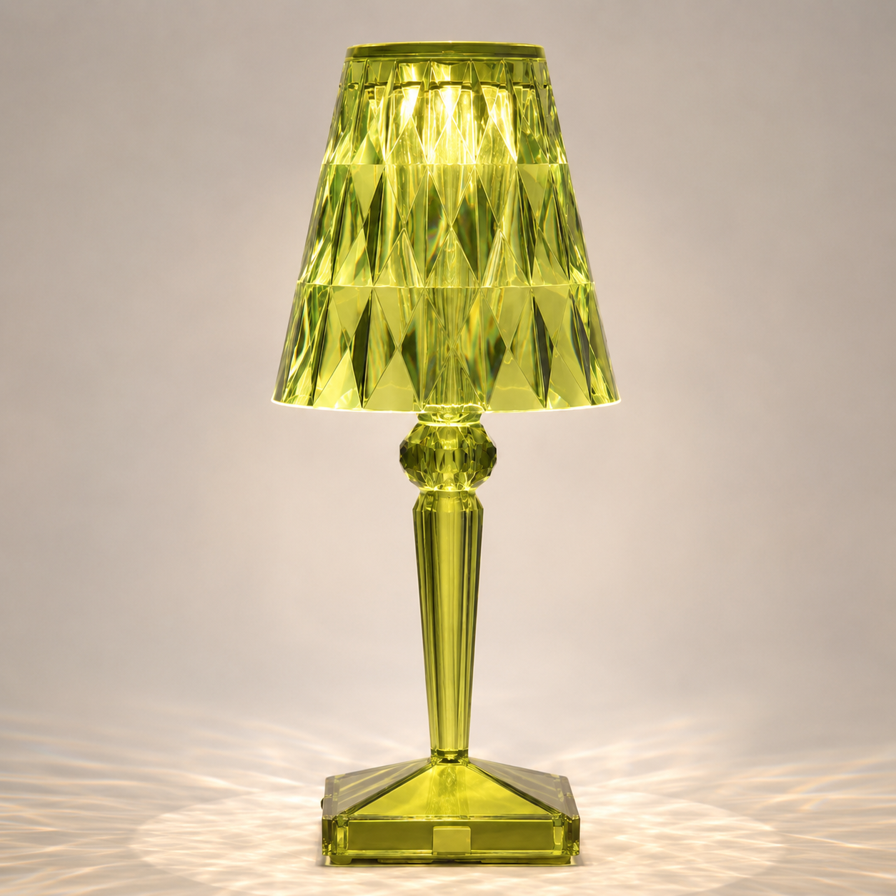 Green transparent table lamp with a faceted shade and square base on a light background.