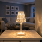 Warm table lamp centered on a living room coffee table with a sofa and framed wall art in the background.