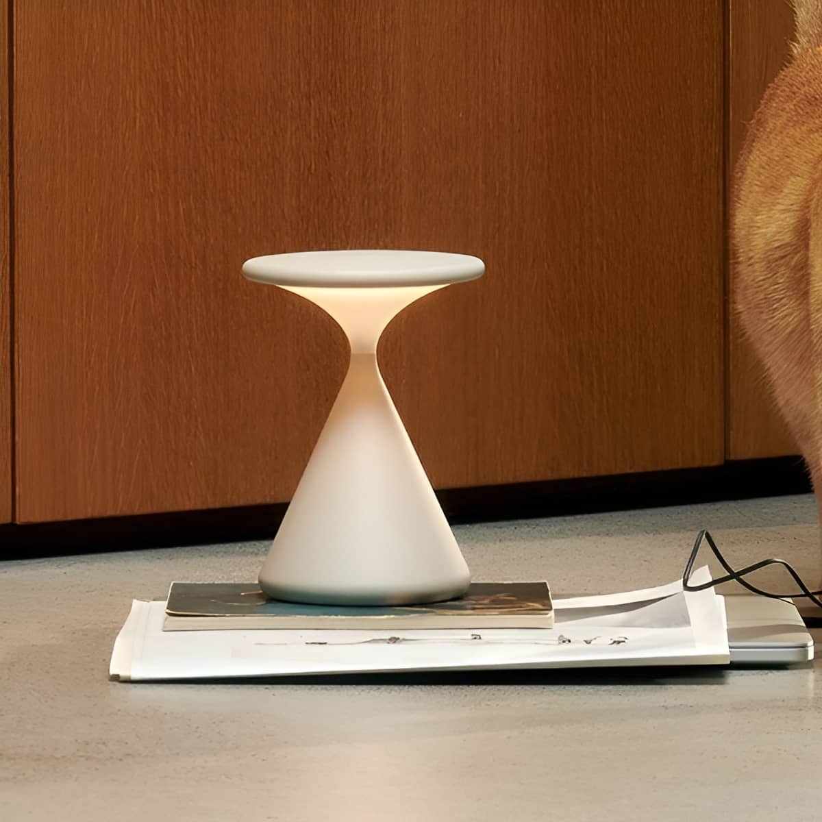 White rechargeable table lamp standing on books beside glasses.