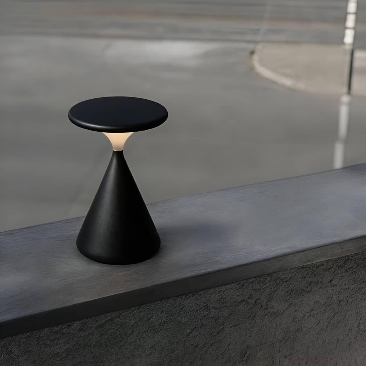 Black rechargeable table lamp on a concrete ledge.