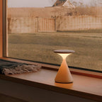 White rechargeable table lamp glowing beside a window at dusk.