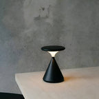 Black rechargeable table lamp on a white surface against a gray wall.