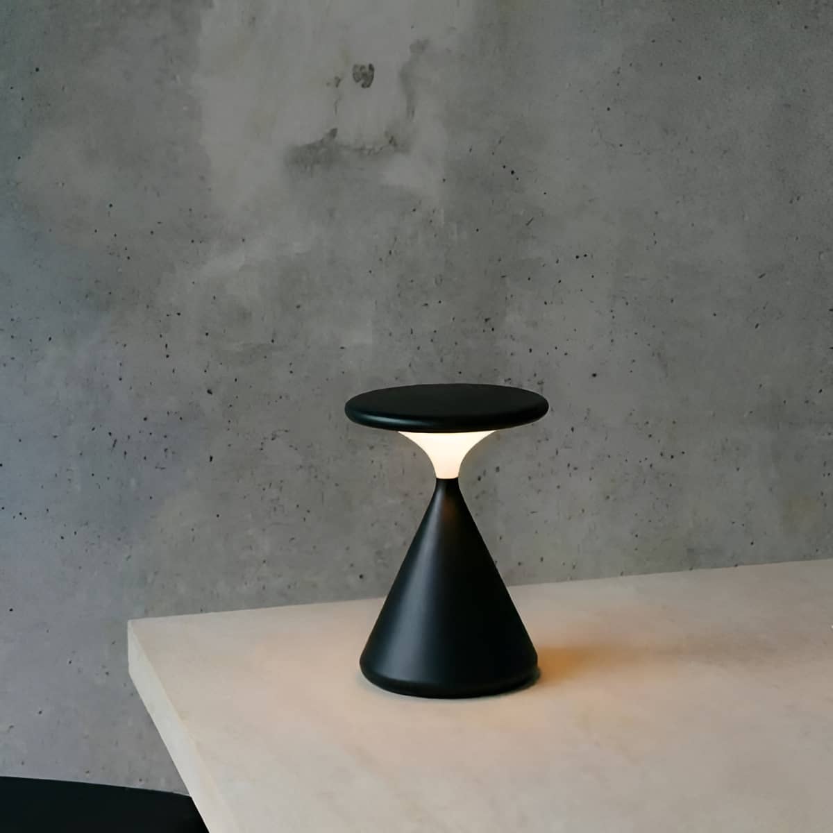 Black rechargeable table lamp on a white surface against a gray wall.