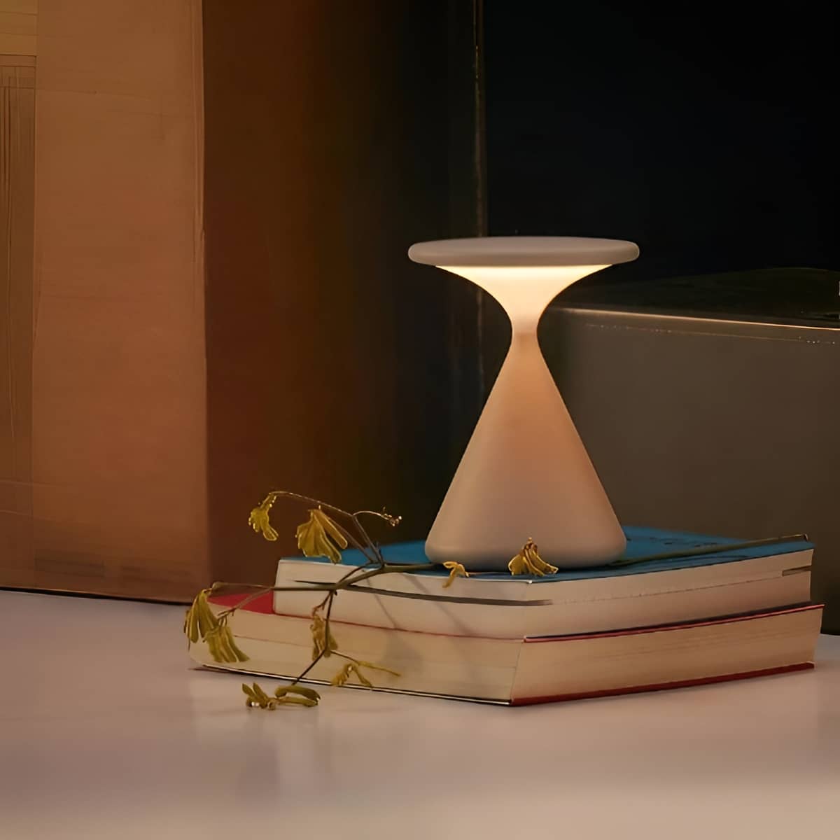 White rechargeable table lamp glowing on a stack of books.