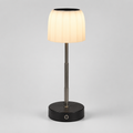 A modern table lamp with a pleated white fabric shade, a brushed metal stem, and a round black base on a light gray background.