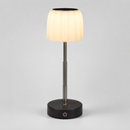 A modern table lamp with a pleated white fabric shade, a brushed metal stem, and a round black base on a light gray background.