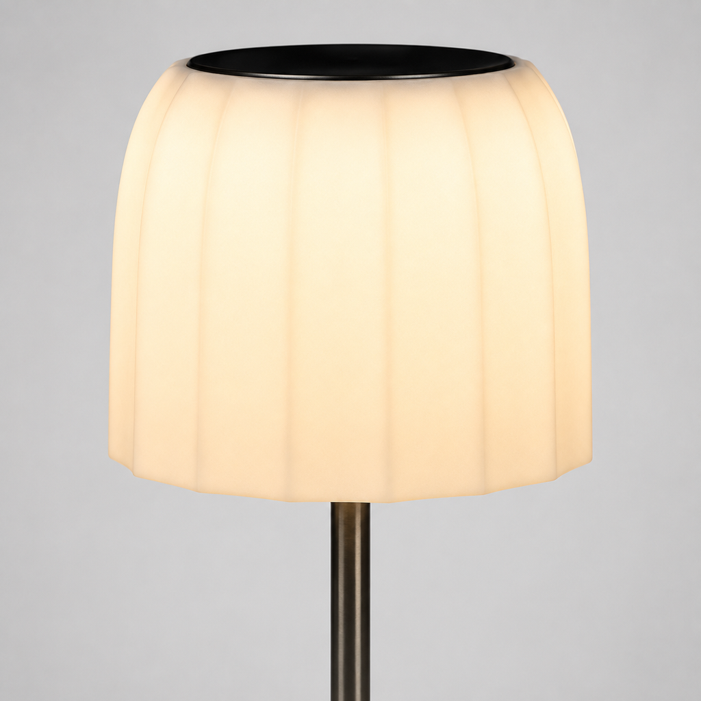 A modern table lamp with a pleated, fluted white shade that glows warm yellow when lit, supported by a slim dark metal stem against a neutral gray background.