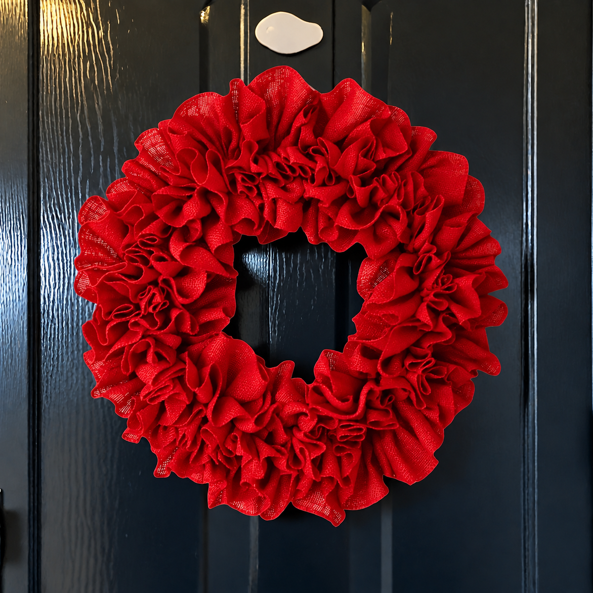 Red ruffle Christmas wreath hanging on a dark door with a heart shaped hook