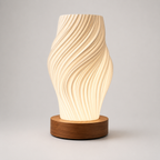 A modern table lamp with a sculptural, wavy ribbed shade in a warm cream color, resting on a round, dark brown wooden base against a neutral light gray background.