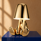 Gold thinker table lamp in the Mr. What pose on a cobalt plinth