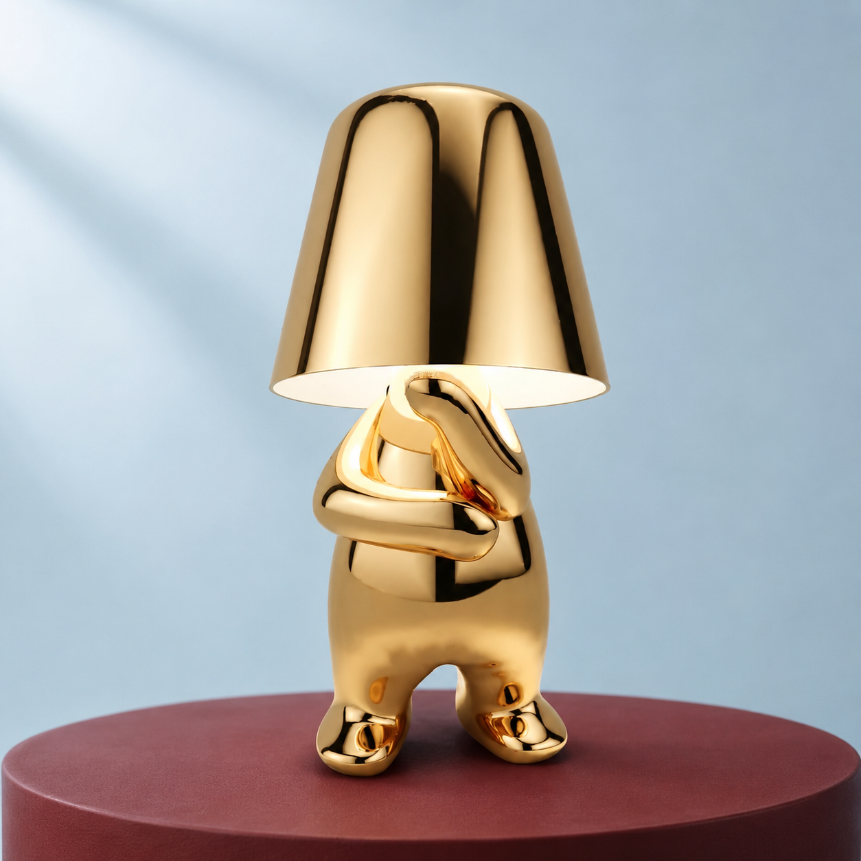 Gold thinker table lamp in the Mr. Why pose on a burgundy pedestal