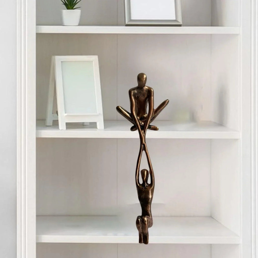 Bronze paired figure sculpture hanging from a white shelving unit