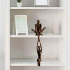 Bronze paired figure sculpture hanging from a white shelving unit