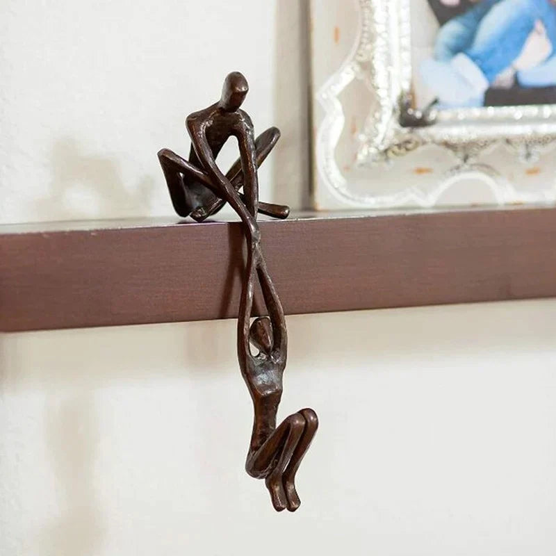 Dark resin figures holding hands below a shelf edge