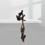 Black resin sculpture with seated and hanging figures on a white shelf