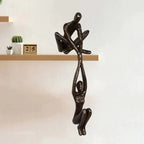 Black paired figure sculpture beside decorative objects on a wood shelf